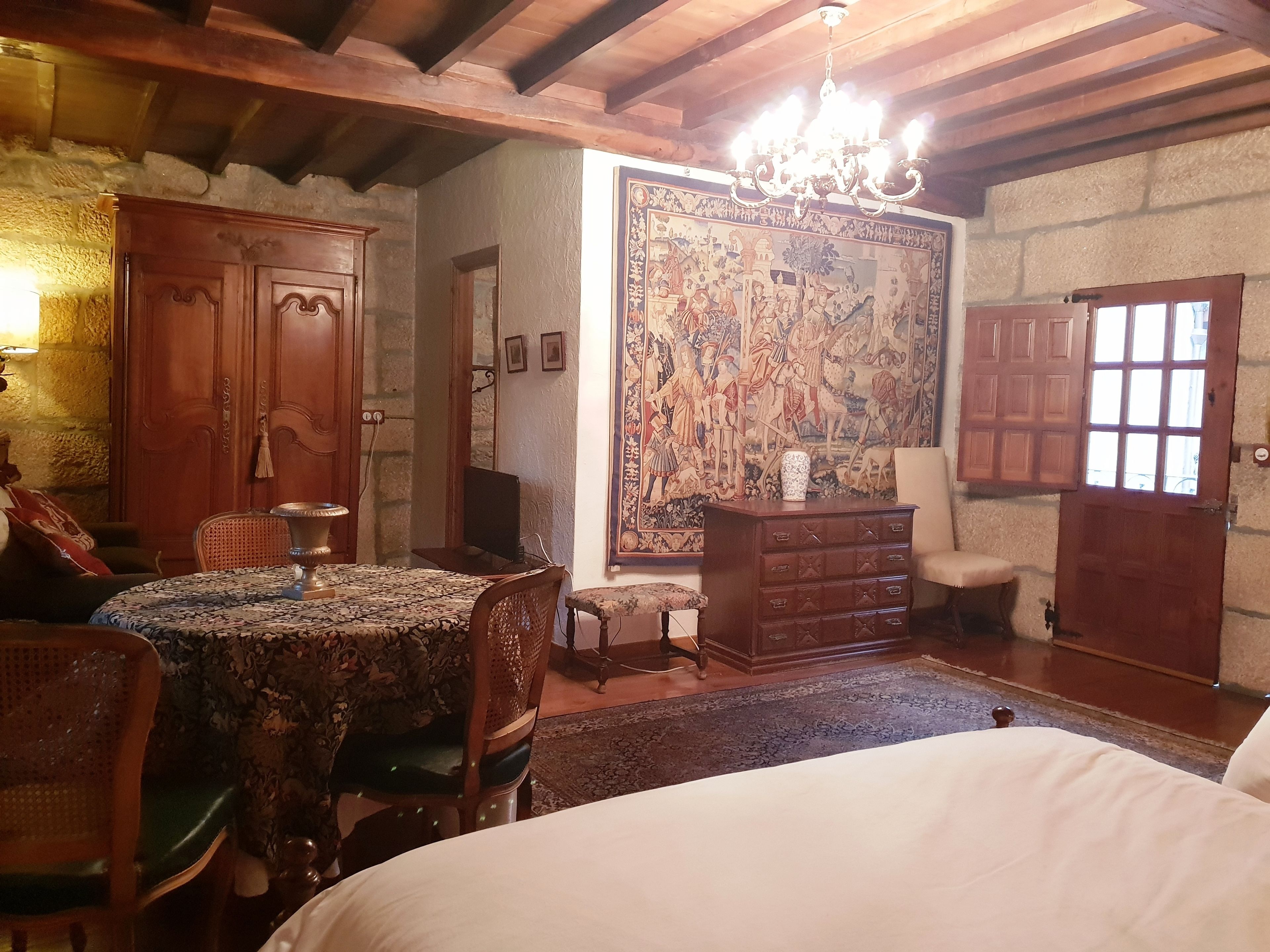 A traditional room with a wooden ceiling, a large tapestry, a chandelier, and a bed.