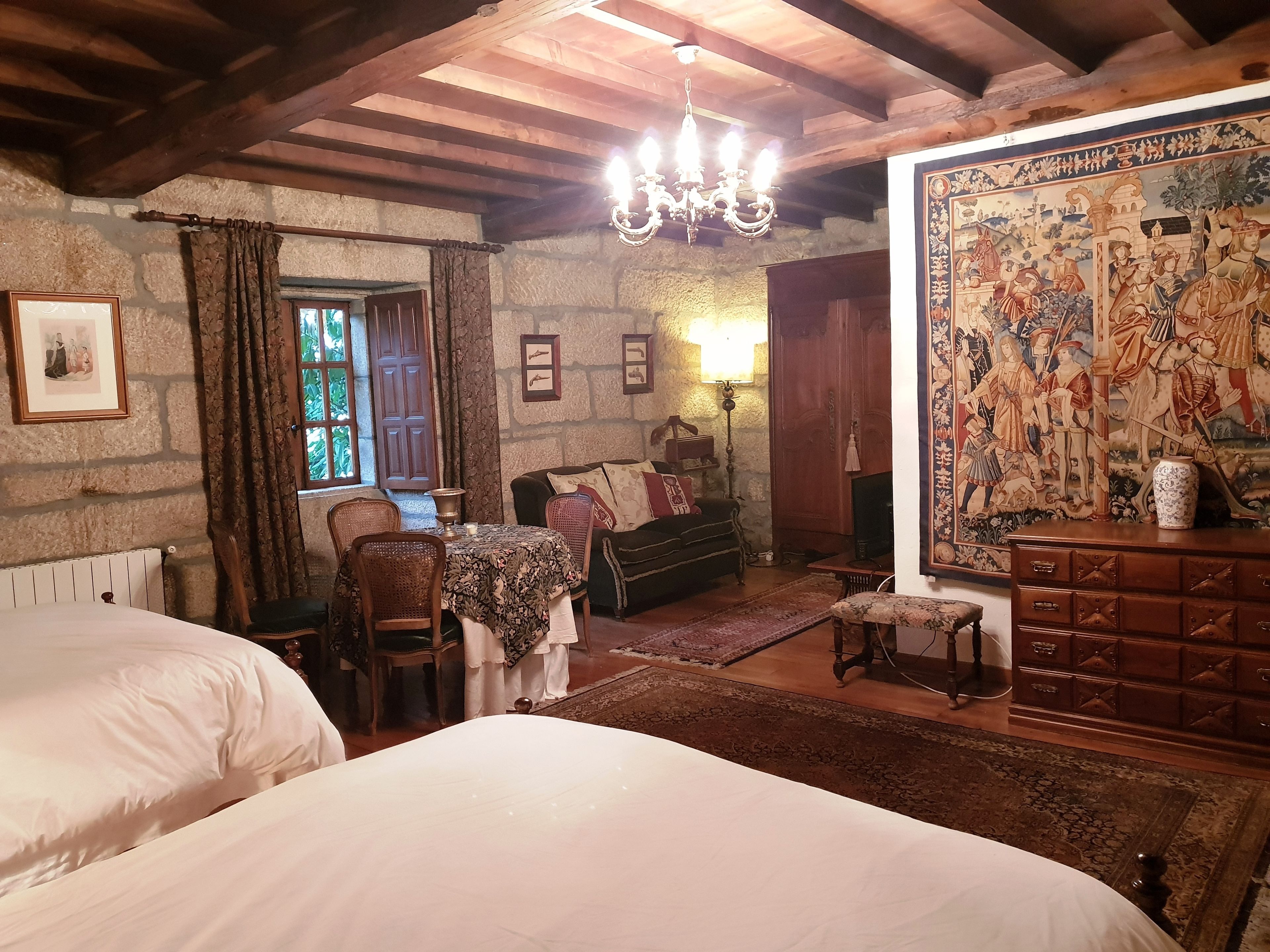 Una habitación tradicional con paredes de piedra, vigas de madera, un candelabro, un tapiz y una chimenea.