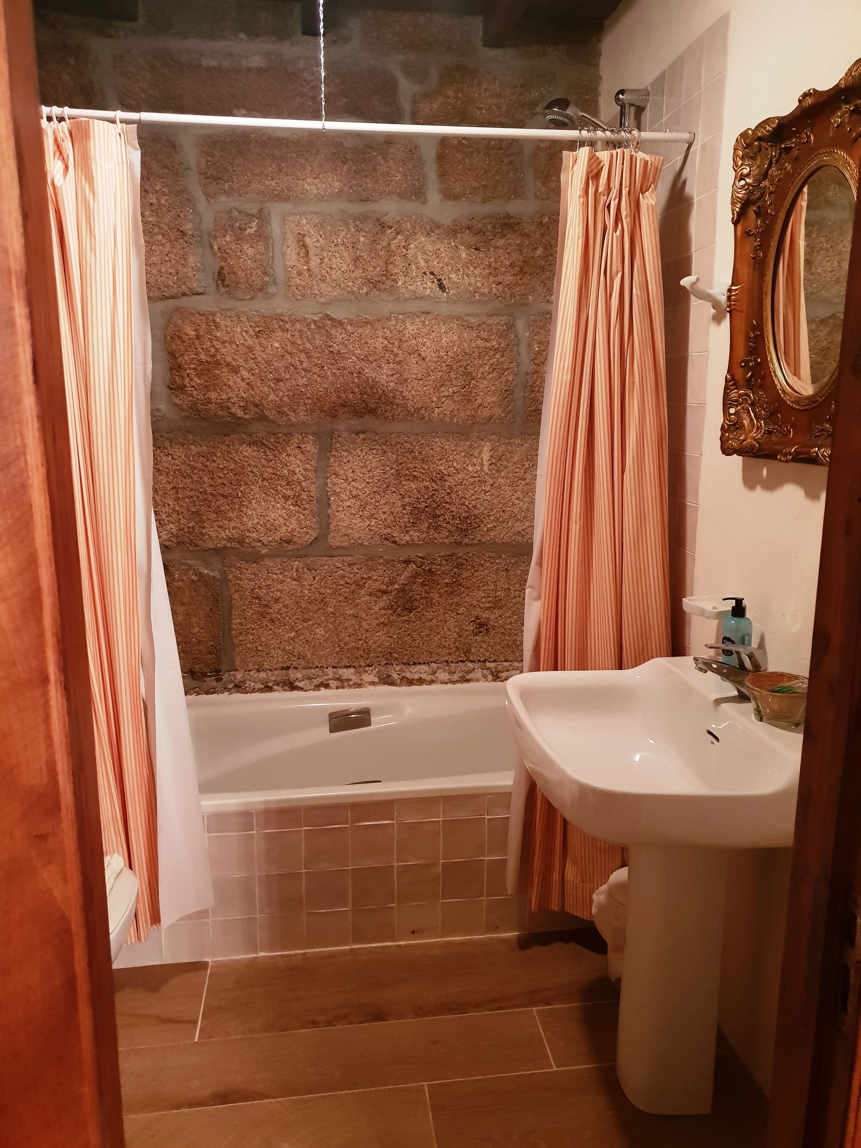 Une salle de bain avec un mur en pierre, une baignoire, un lavabo et un miroir.