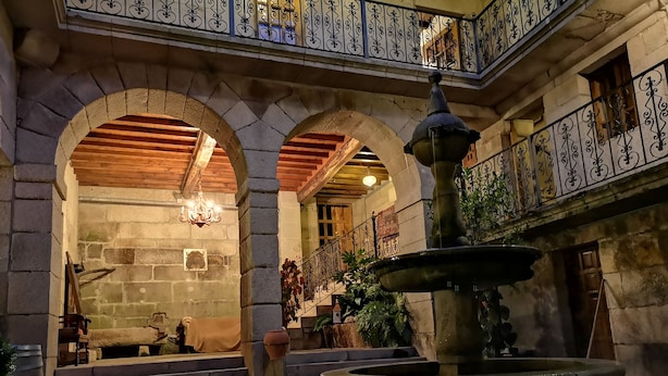 Un patio con una fuente, arcos de piedra y una escalera de madera.