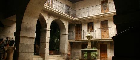 Une cour avec une fontaine, des arches en pierre et une porte en bois.