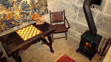 Una habitación con un tablero de ajedrez sobre una mesa, una silla, una pared de piedra y una estufa de leña.