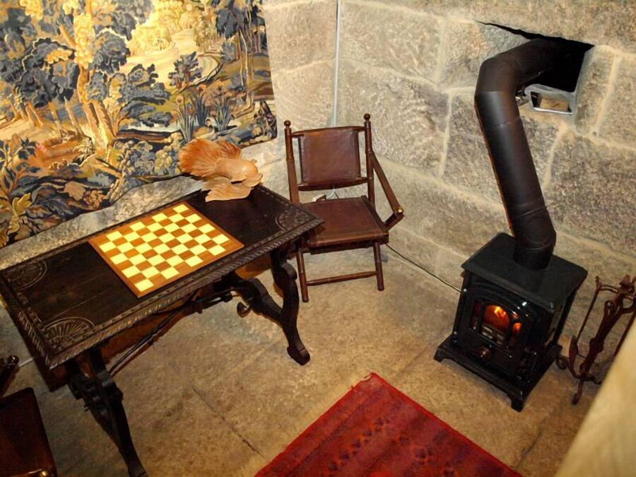 Una habitación con un tablero de ajedrez sobre una mesa, una silla, una pared de piedra y una estufa de leña.