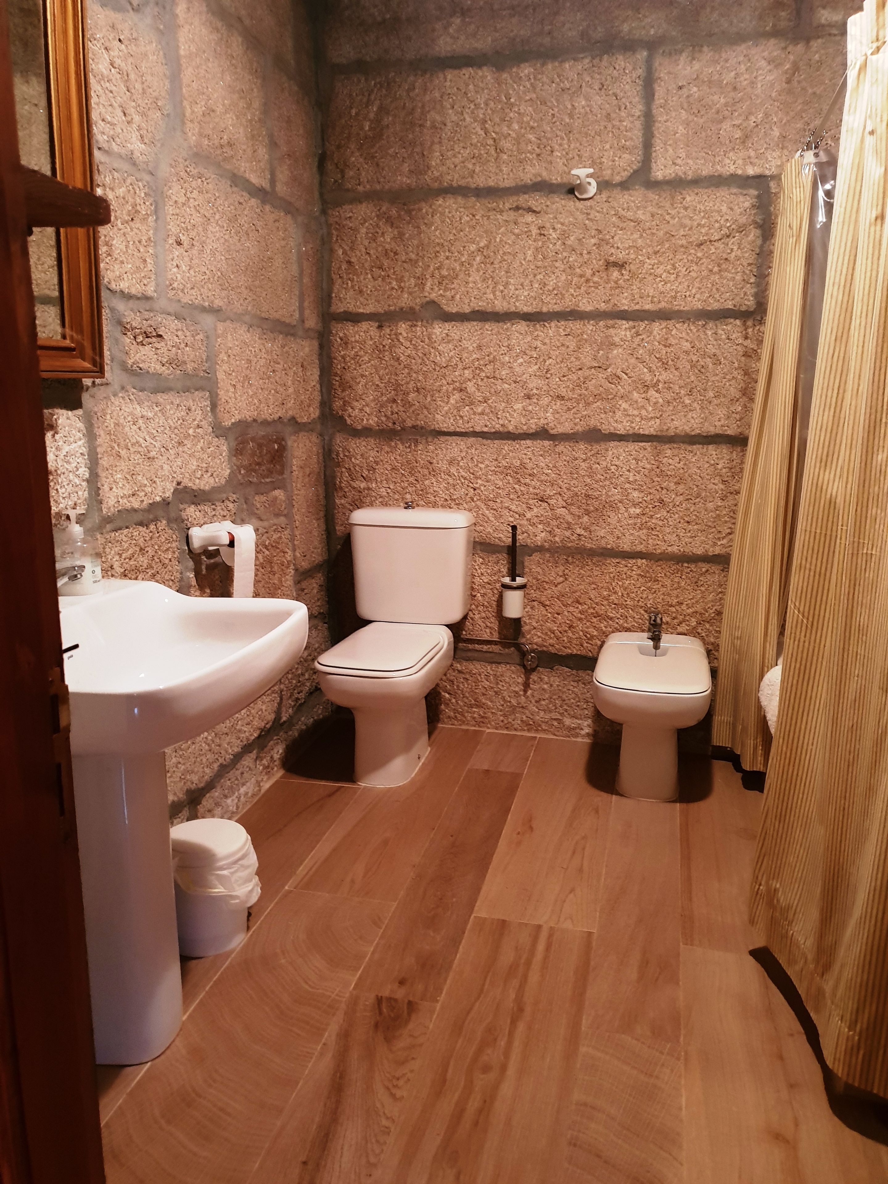 A bathroom with a stone wall, a sink, a toilet, and a bidet.
