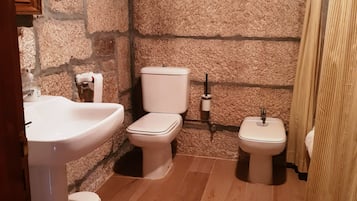 A bathroom with a stone wall, a sink, a toilet, and a bidet.