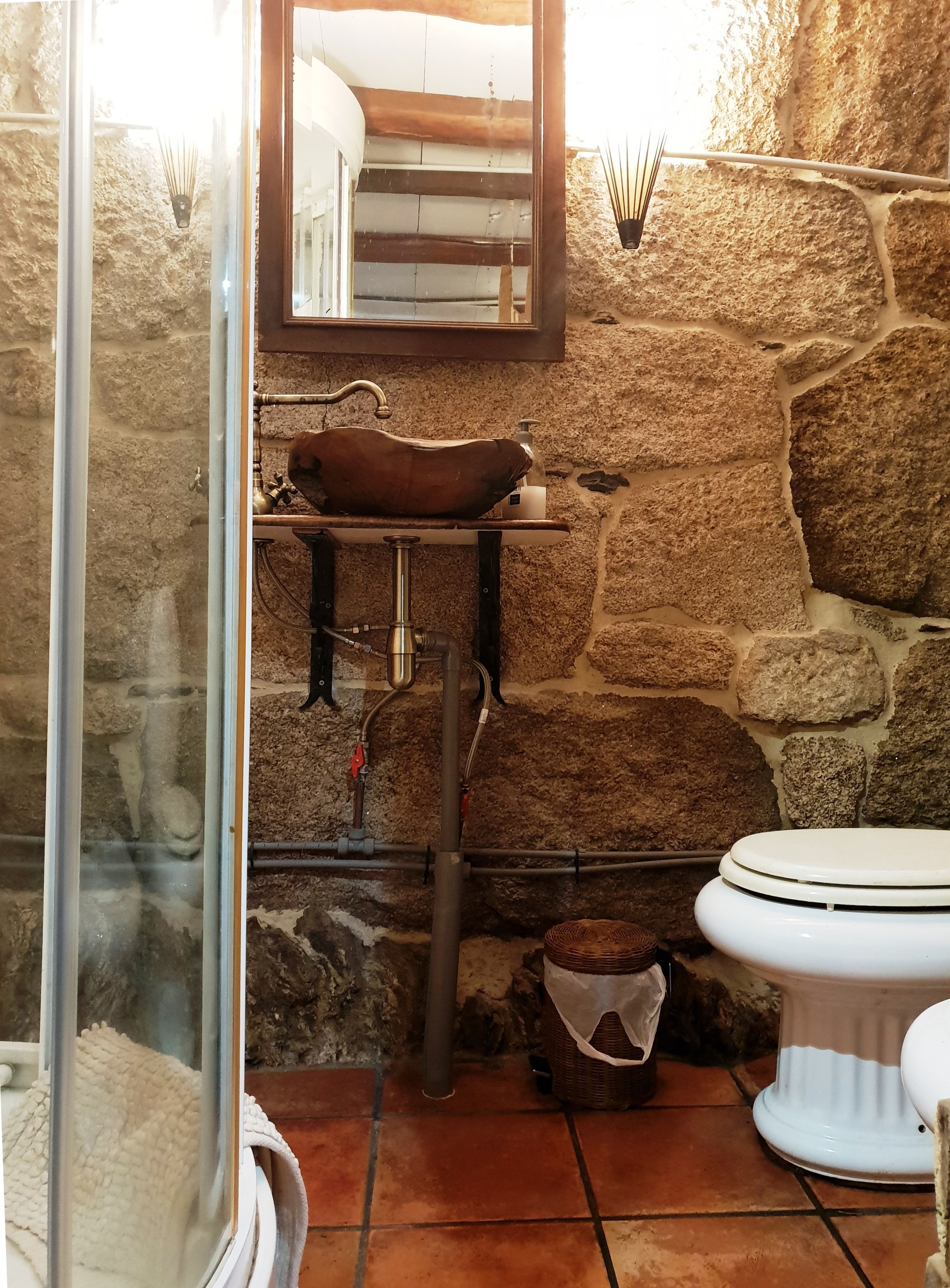 Ein rustikales Badezimmer mit Steinwand, Waschbecken aus Holz und Toilette in Weiß.