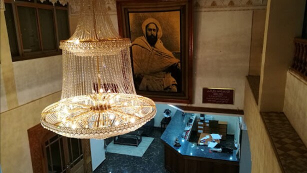 A chandelier, a framed portrait, and a counter with items on it. - Hotel Bouazza (Tiaret)