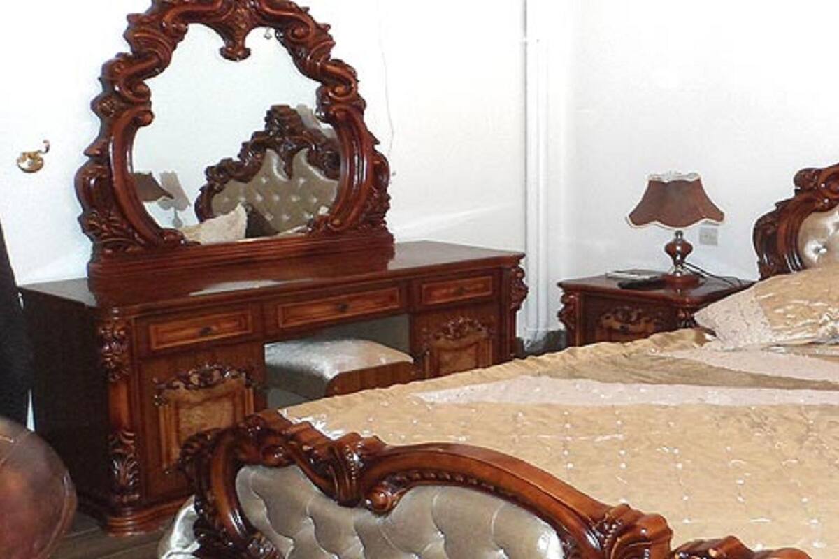 Een slaapkamer met een groot bed, een houten dressoir, een spiegel en een nachtkastje met een lamp.