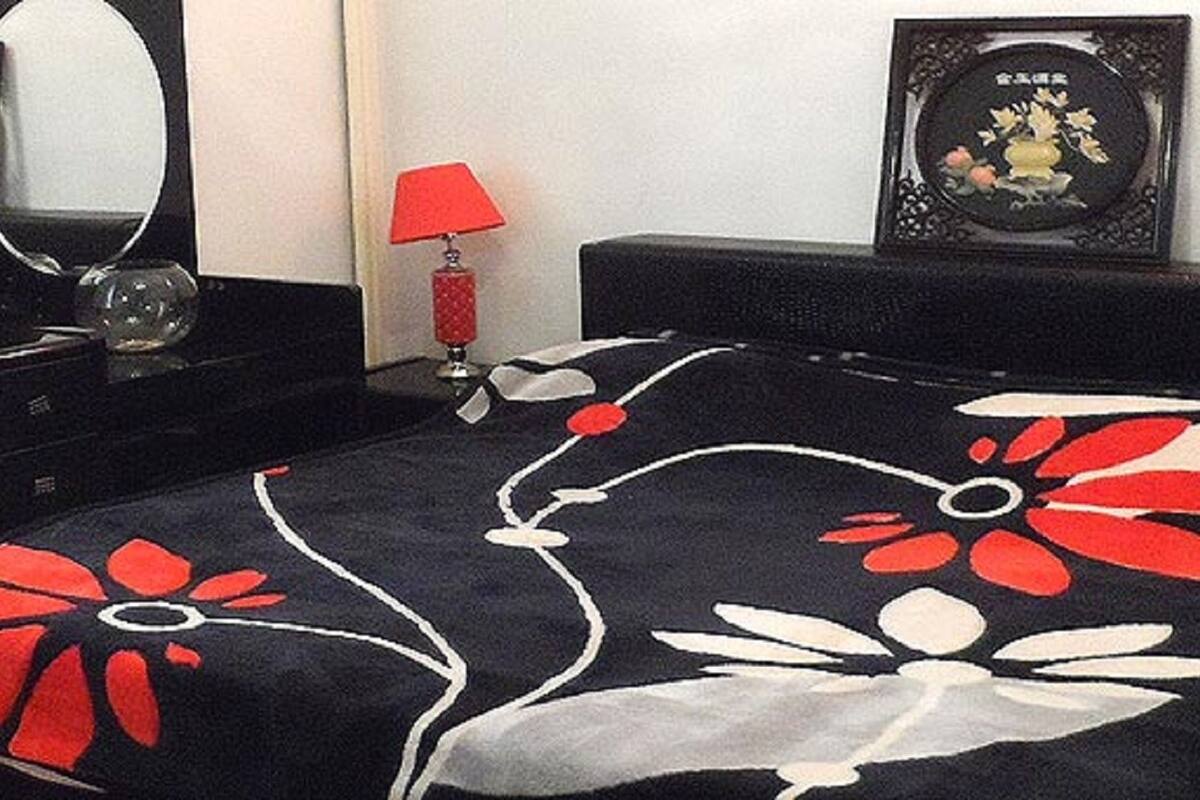 Een bed met een zwart-rode bloemenprint, een spiegel, een rode lamp en een ingelijst beeld aan de muur.