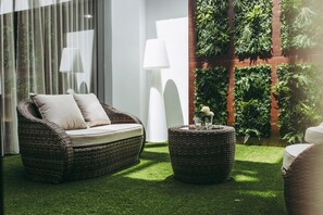 A wicker sofa with cushions, a round wicker table with a vase, and a vertical garden wall. - Masa Hotel 5 de Outubro (Lisbon)