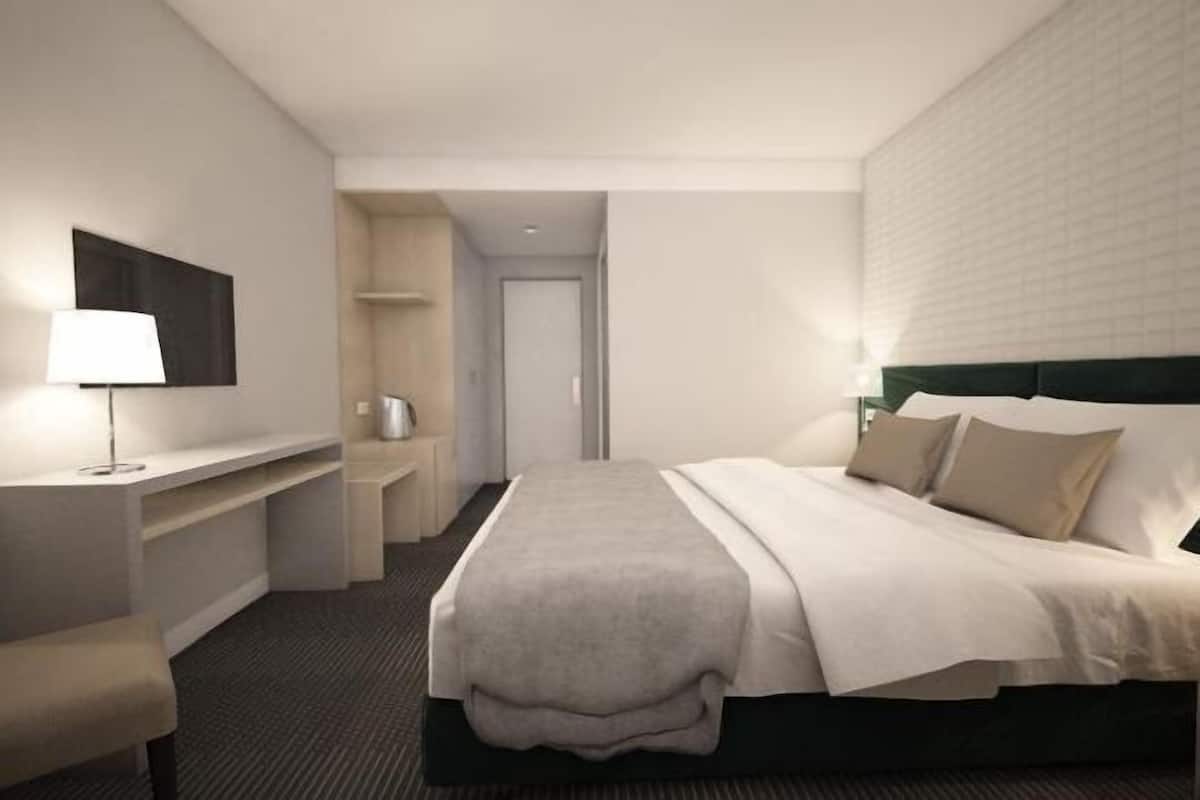 A modern hotel room with a bed, bedside table, lamp, and a flat-screen TV mounted on the wall.