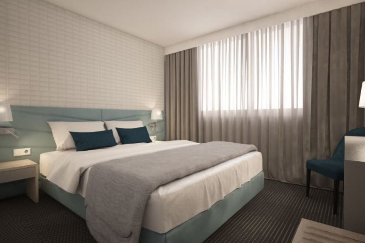 A modern hotel room with a large bed, a nightstand, a desk, and a chair.