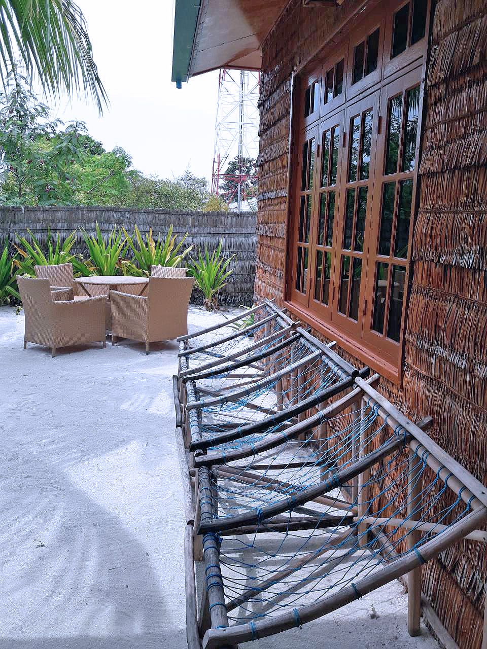 Un edificio con fachada de paja, una ventana de múltiples cristales y una zona de estar con mobiliario de mimbre.