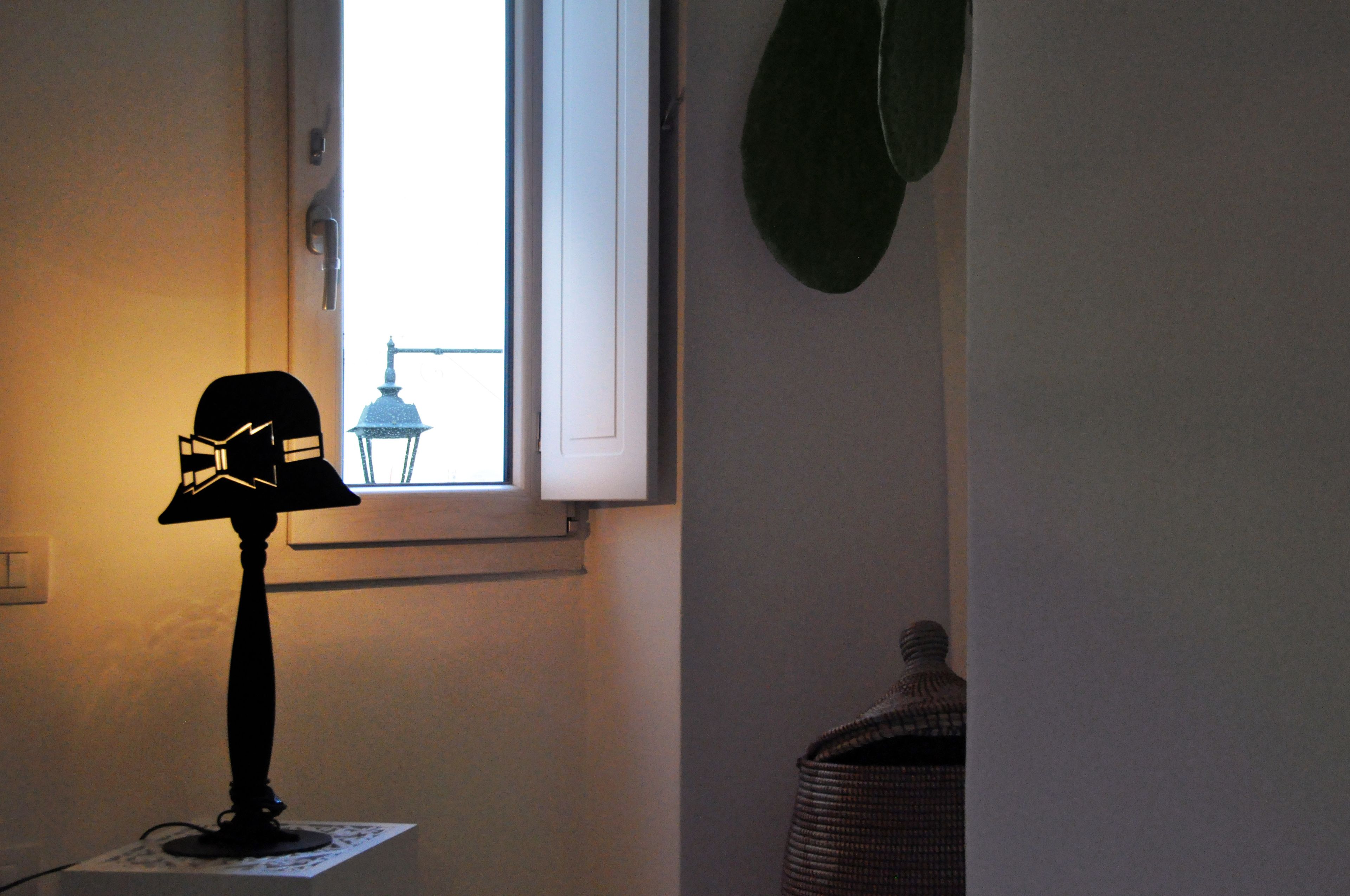 A room with a lamp on a table, a window, and a basket.