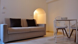 Een woonkamer met een bank, twee stoelen, een tafel en een wandlamp.