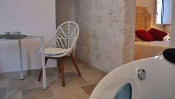 A room with a white chair, a small table with cups, and a bed with red pillows.