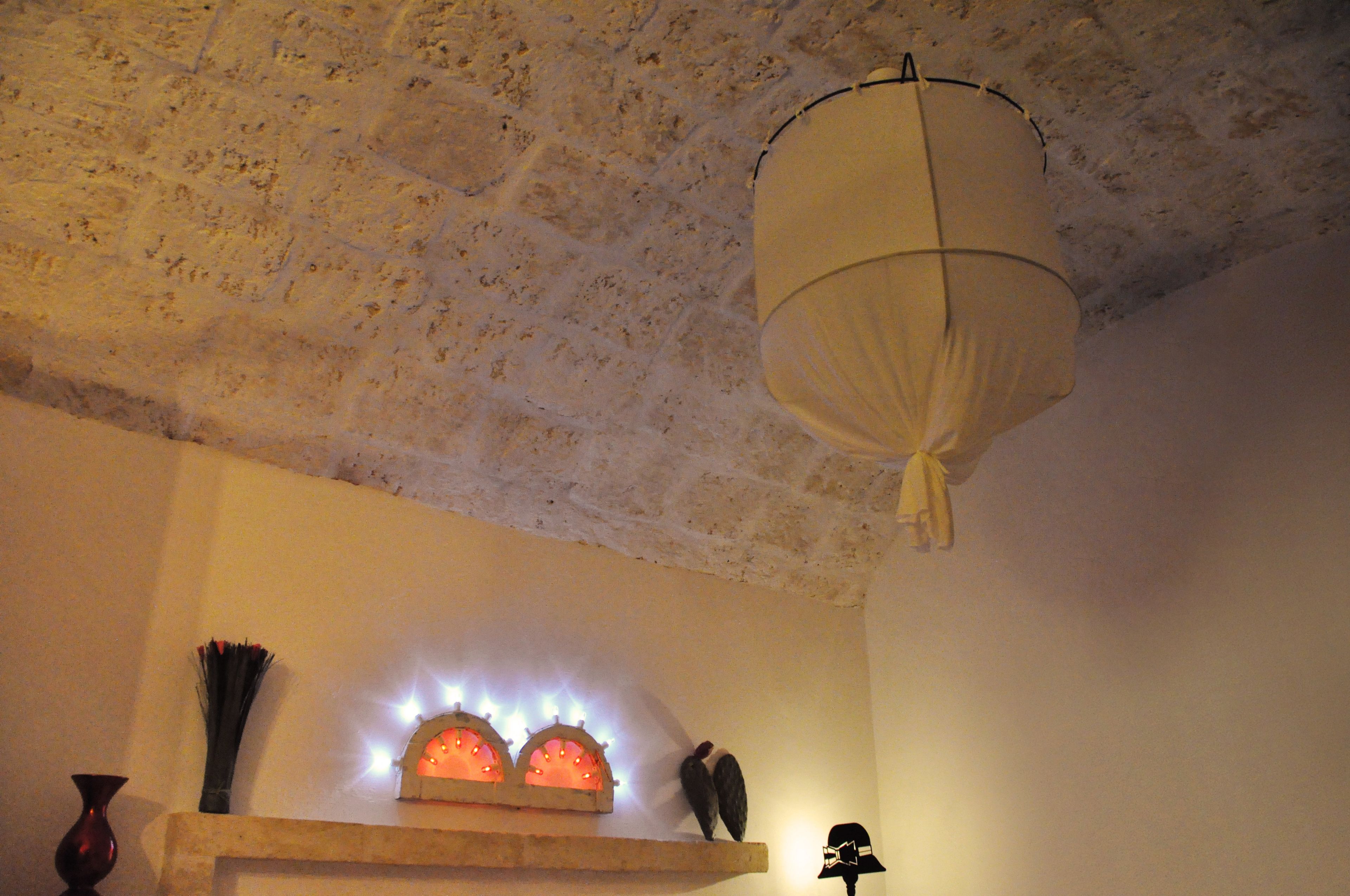 Una habitación con techo texturizado, lámpara colgante, estante con adornos y un reloj en la pared.