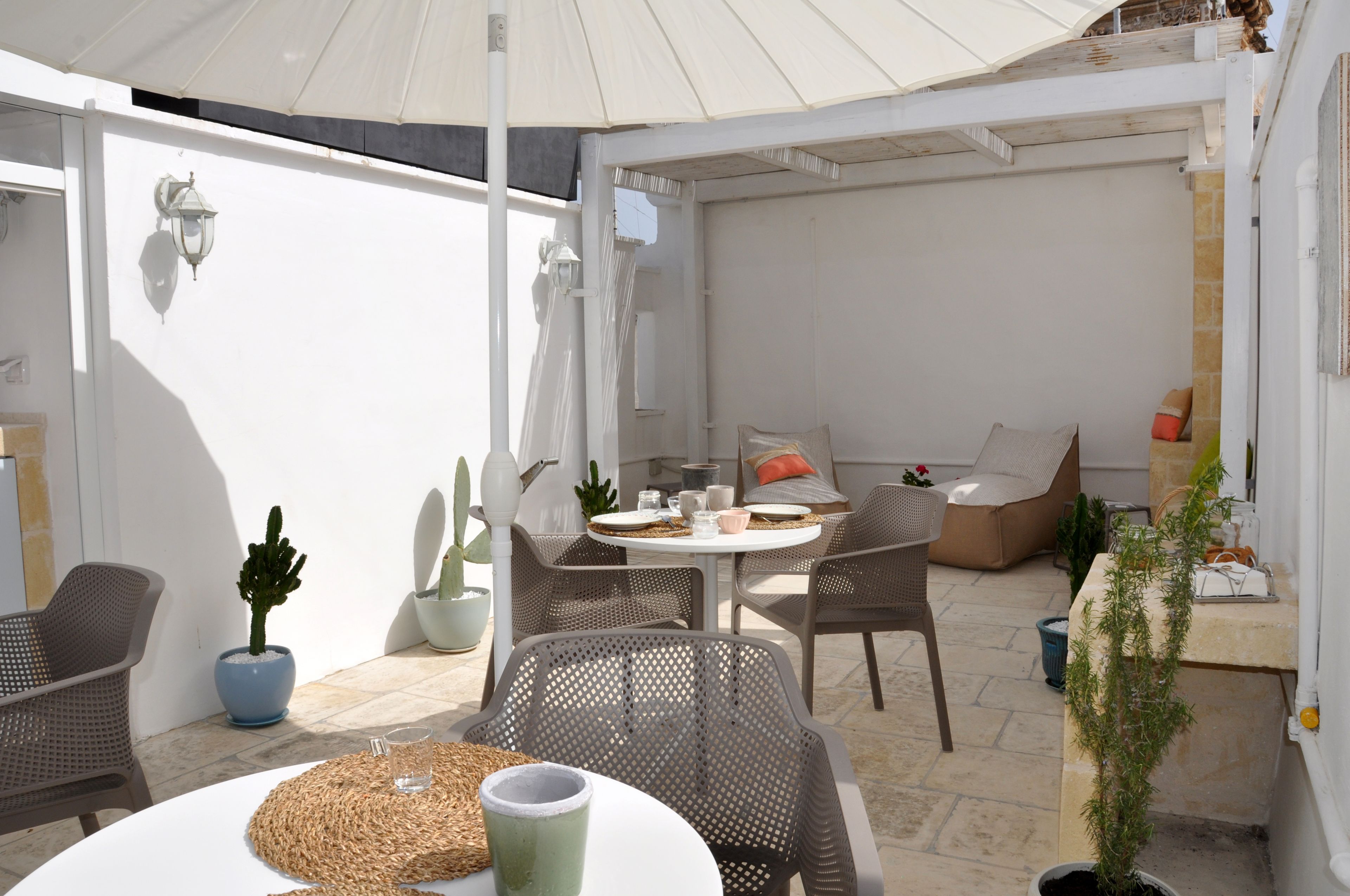 Eine Terrasse mit Korbstühlen, einem runden Tisch und Blumentöpfen.