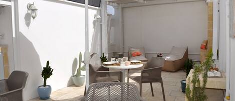 Eine Terrasse mit Korbstühlen, einem runden Tisch und Blumentöpfen.