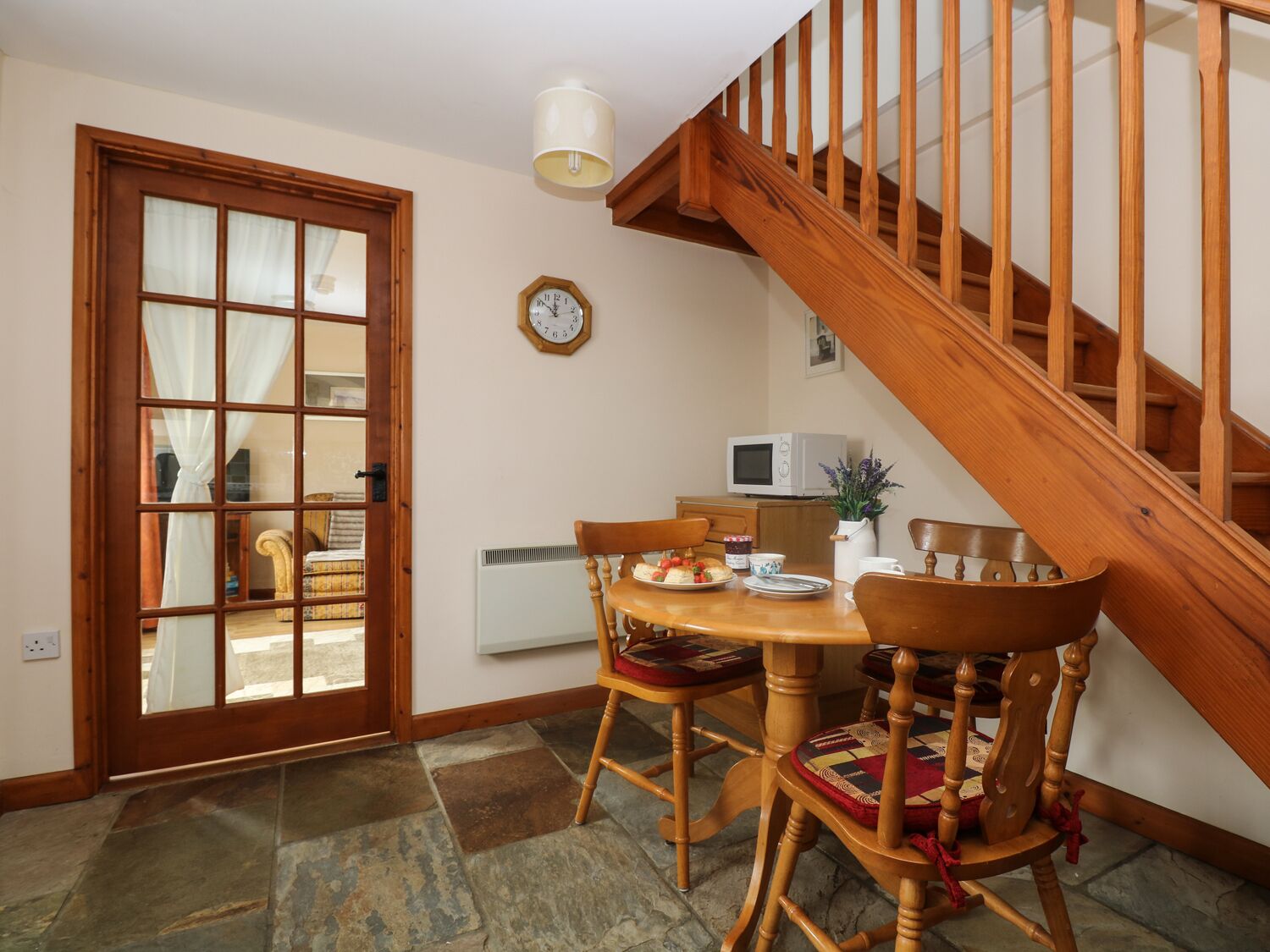 A dining area with a wooden table, chairs, a clock, and a staircase.