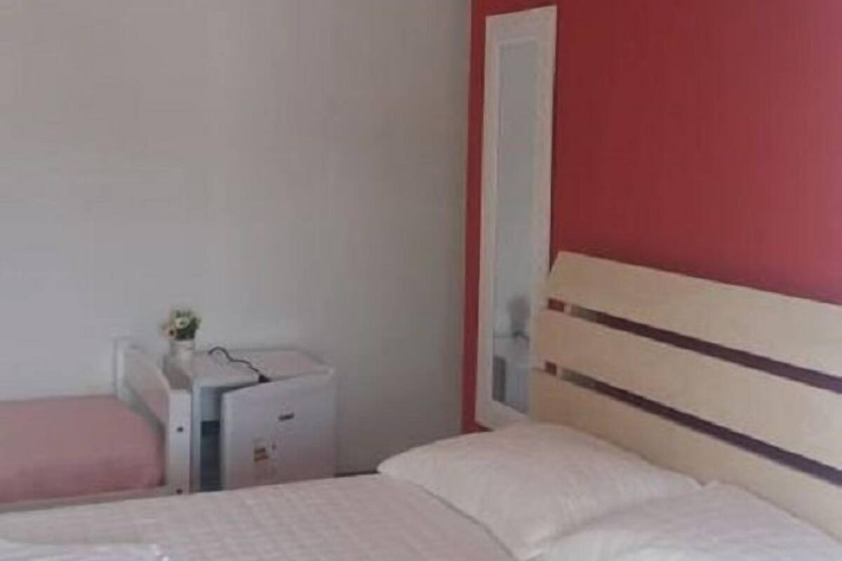 A bedroom with a bed, a bedside table, a mirror, and a red wall.