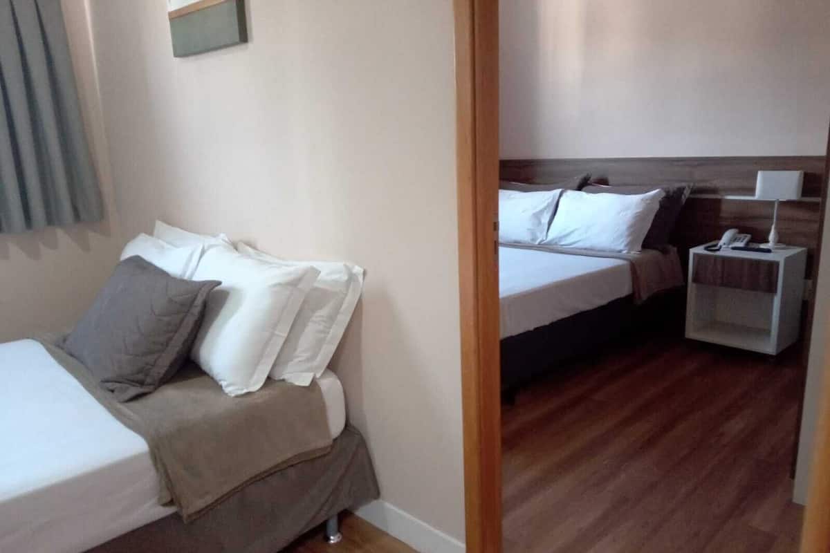Une chambre avec deux lits, chacun agrémenté de draps et d’oreillers blancs, une table de chevet avec une lampe et un plancher en bois.