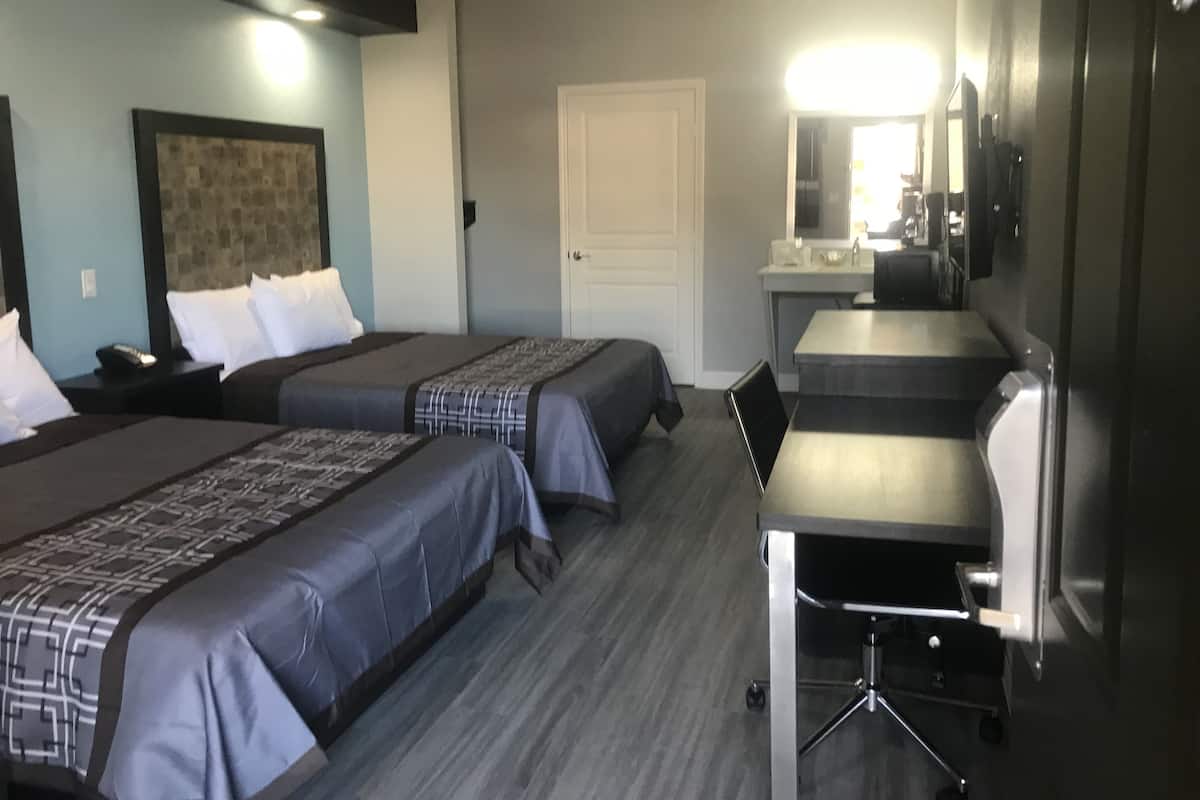Habitación de hotel con dos camas, un escritorio, una silla, un televisor y la puerta del baño.