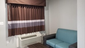 A living room with a blue sofa, a brown and white striped curtain, and a white air conditioning unit. - The Residency Suites (Houston)