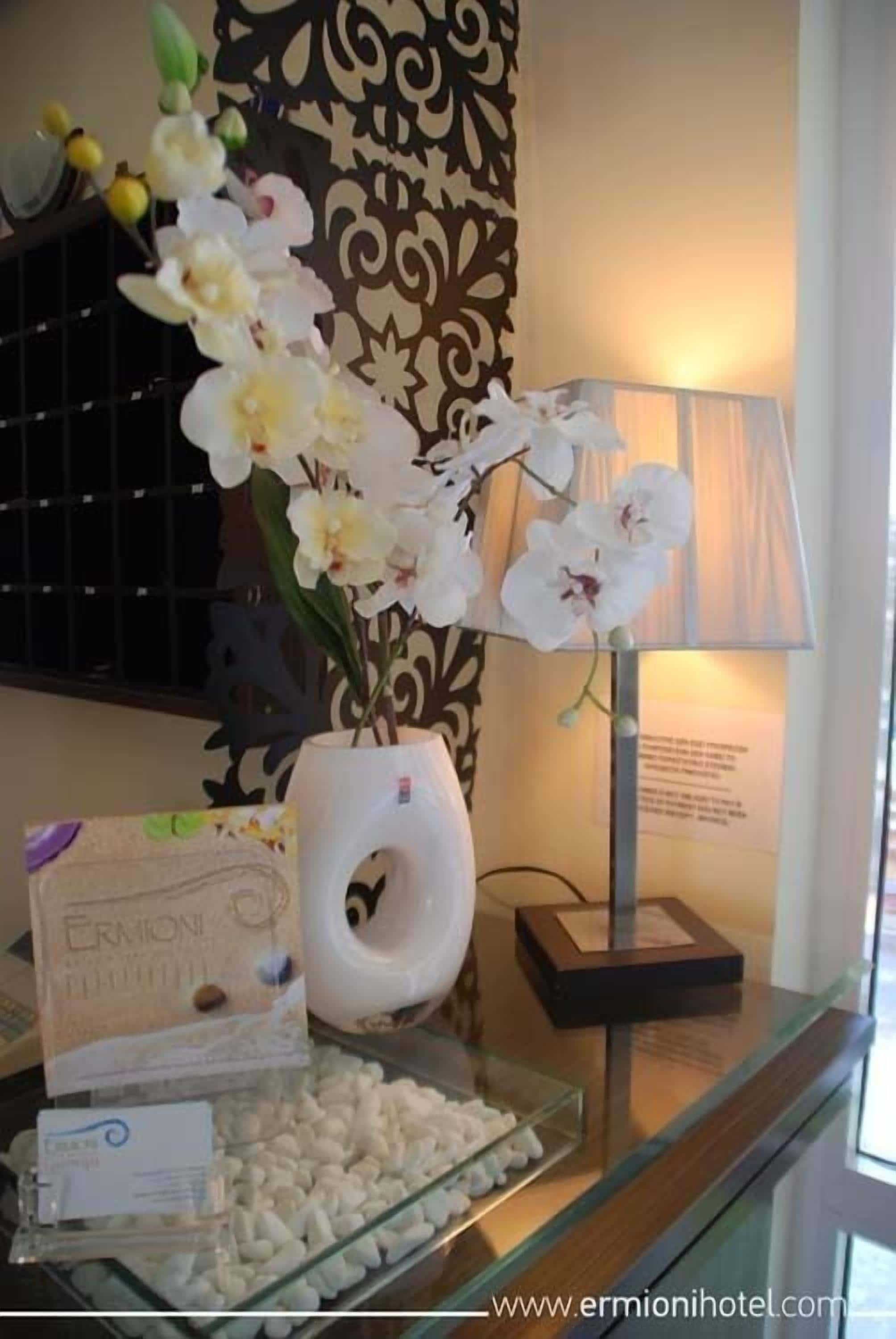 Een receptiegedeelte met een vaas witte orchideeën, een lamp en een glazen vitrine met witte chocolades.