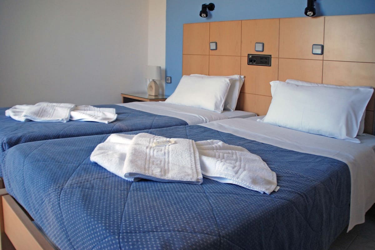 A hotel room with two beds, each with blue bedding and white pillows. There are towels placed on the beds.