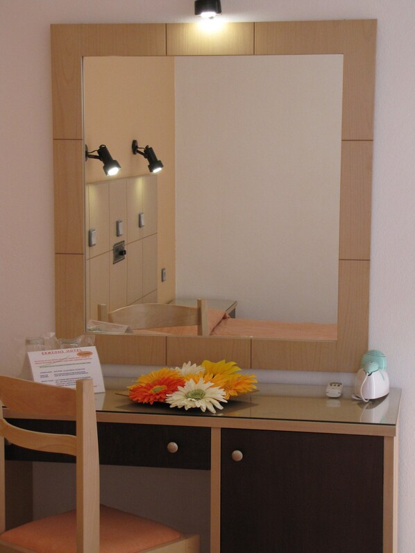 Una habitación de hotel con un escritorio de madera, una silla, un espejo y un arreglo floral.