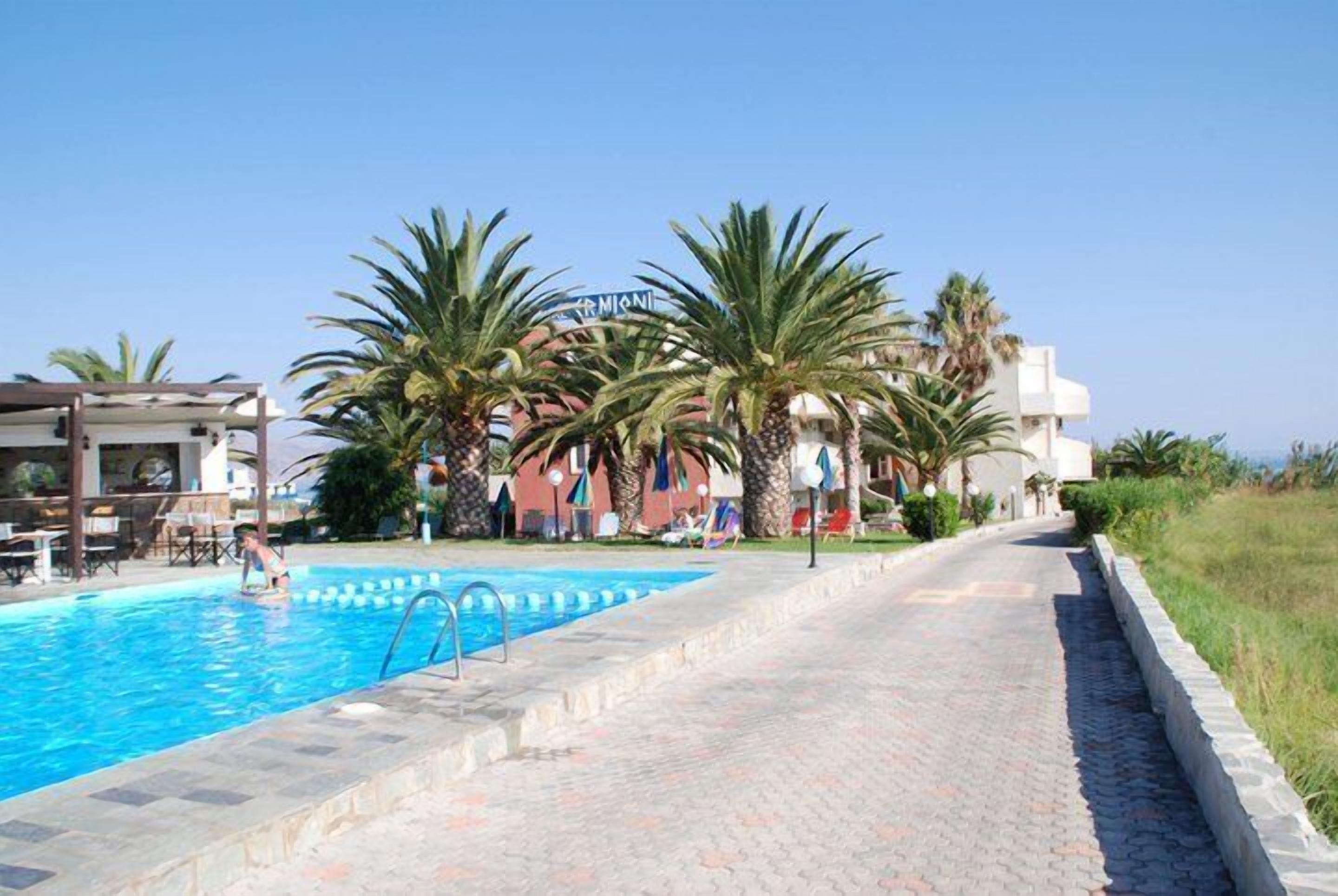 A swimming pool with a clear blue water, surrounded by palm trees and a building with a sign that reads "TRAMONTI".