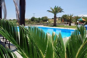 A swimming pool with palm trees and a clear sky. - Ermioni Hotel (Apokoronas)