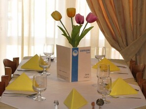 A hotel table set with yellow napkins, wine glasses, and a menu stand labeled "ERMIONI Hotel". - Ermioni Hotel (Apokoronas)
