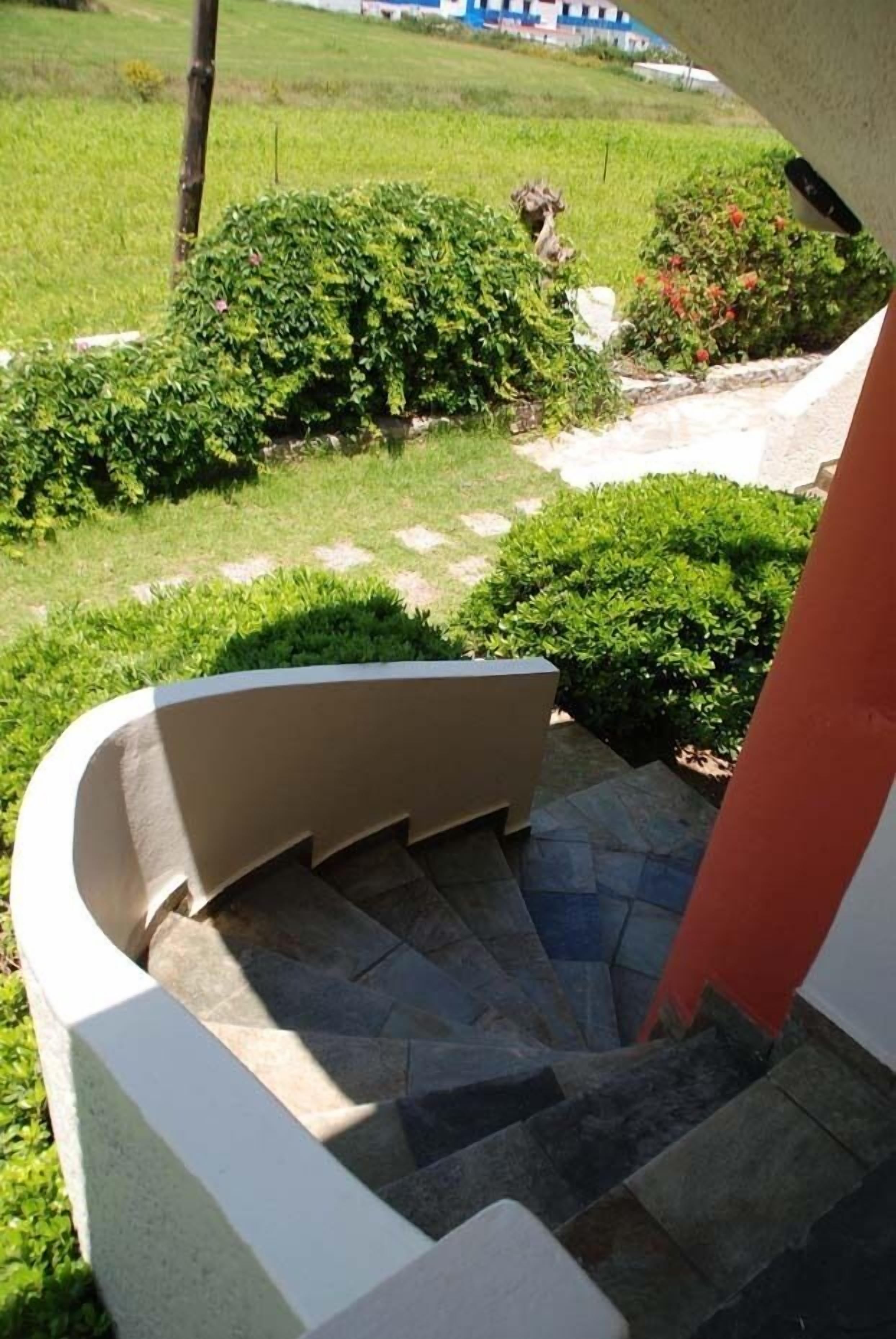 A curved staircase with stone steps leading to a garden area with green shrubs and a lawn.