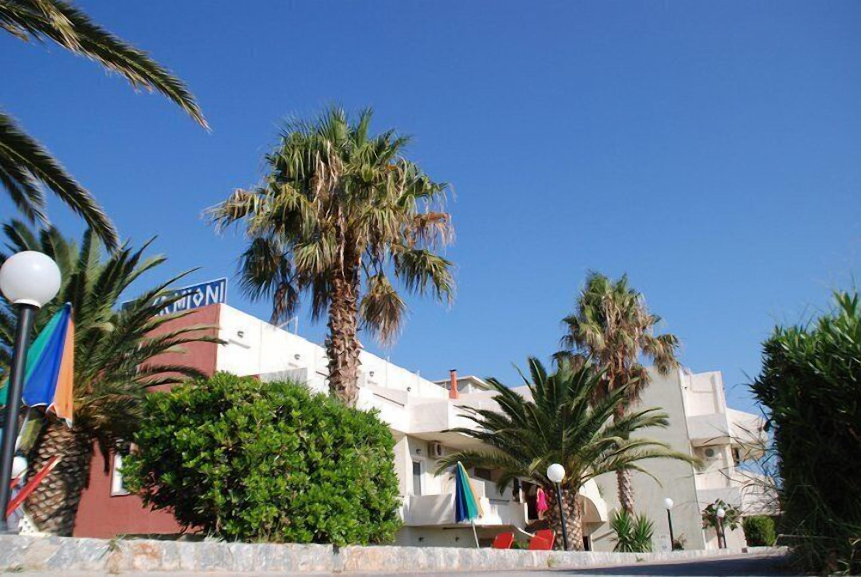 Un hotel de fachada blanca, con palmeras y un cielo azul despejado.