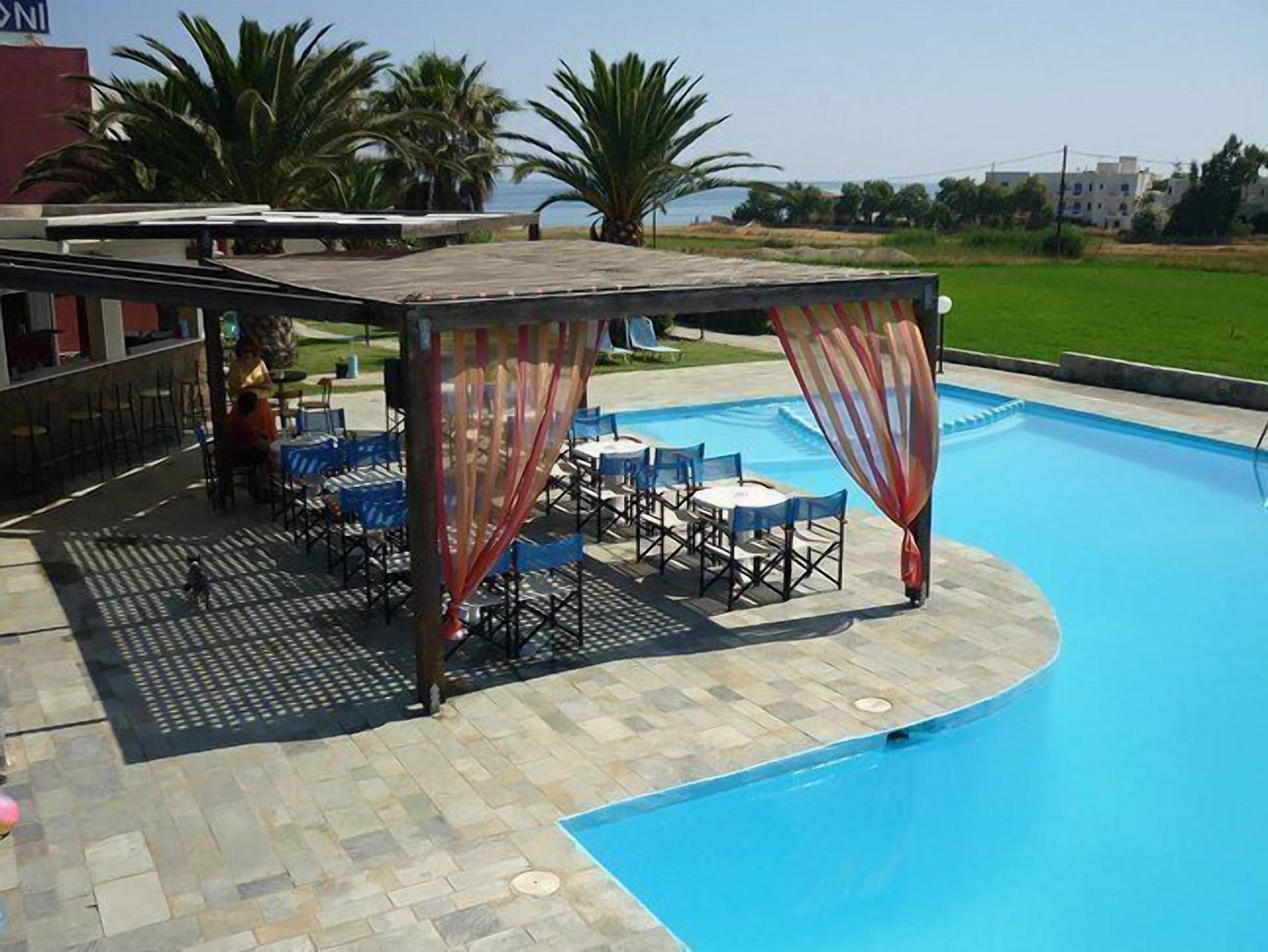 A pool area with a covered seating area and a view of the sea.
