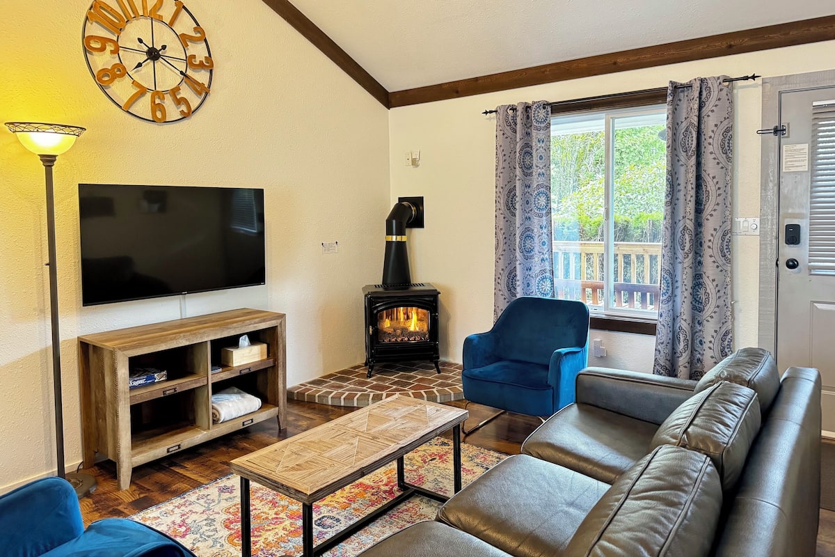A living room with a TV, wooden entertainment unit, blue chair, sofa, and a fireplace.