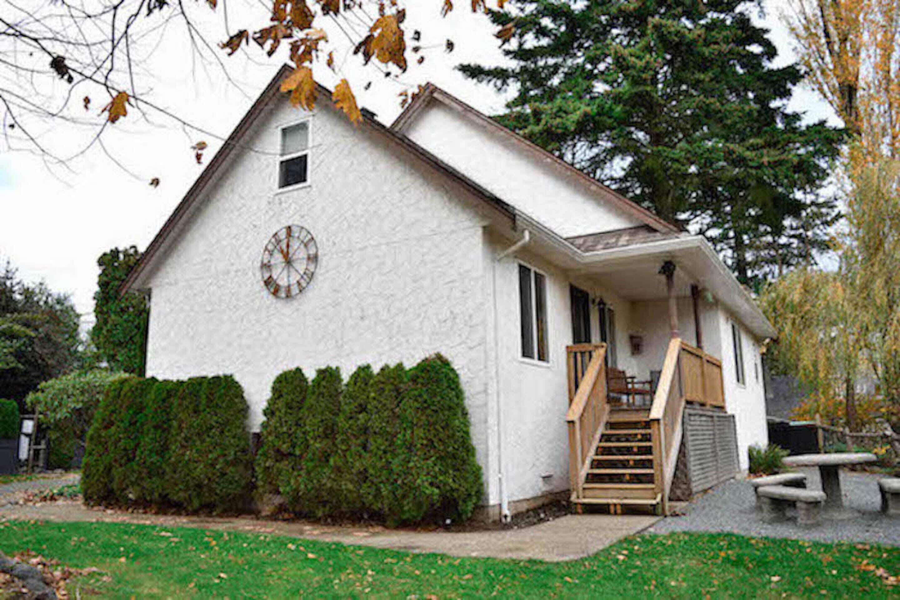 A white building with a clock on the front, a wooden staircase, and a bench outside.