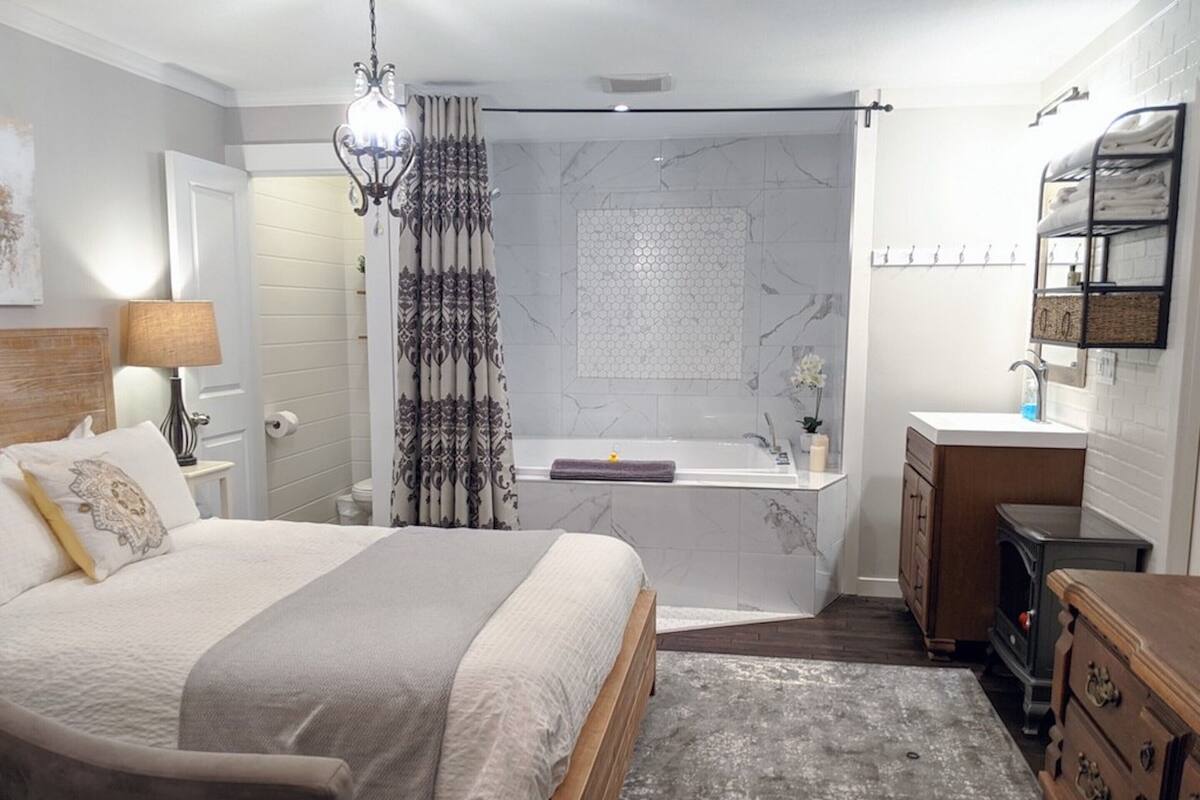 A modern bedroom with a large bed, a bathroom with a bathtub, and a wooden dresser.