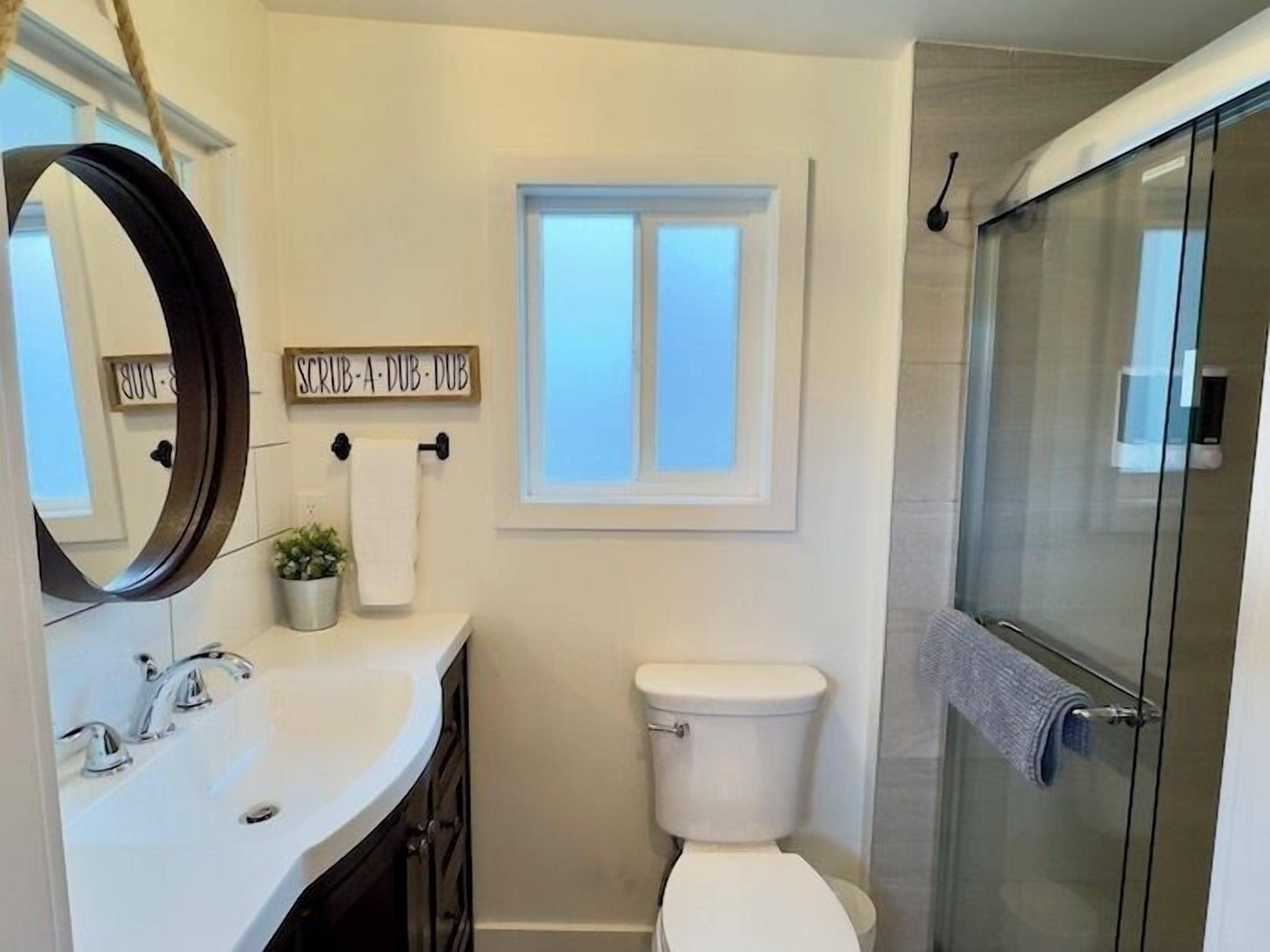 Un bagno con lavandino bianco, WC, doccia e finestra.