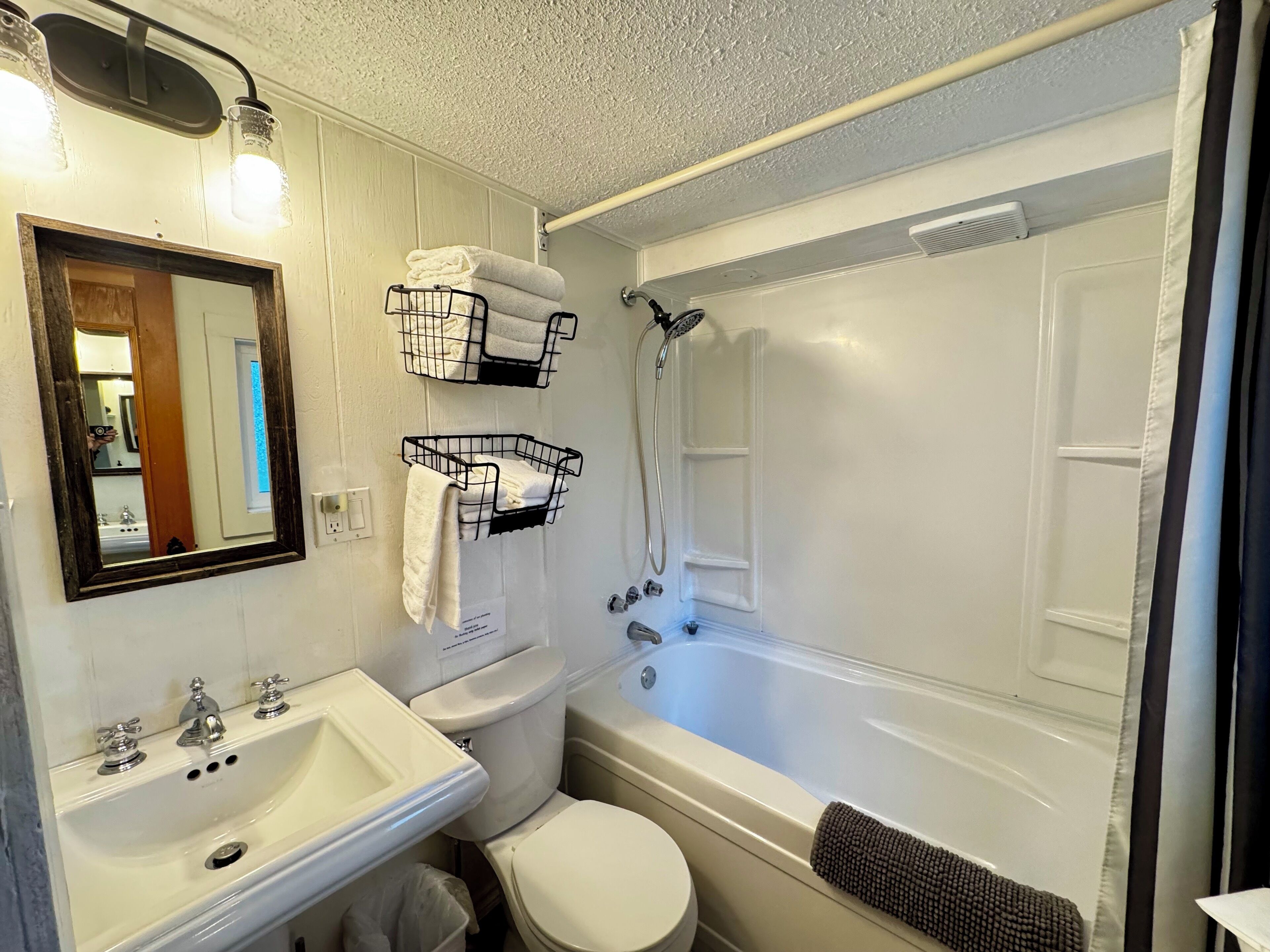 A bathroom with a sink, toilet, and bathtub. There are towel racks above the sink and a shower curtain over the bathtub.