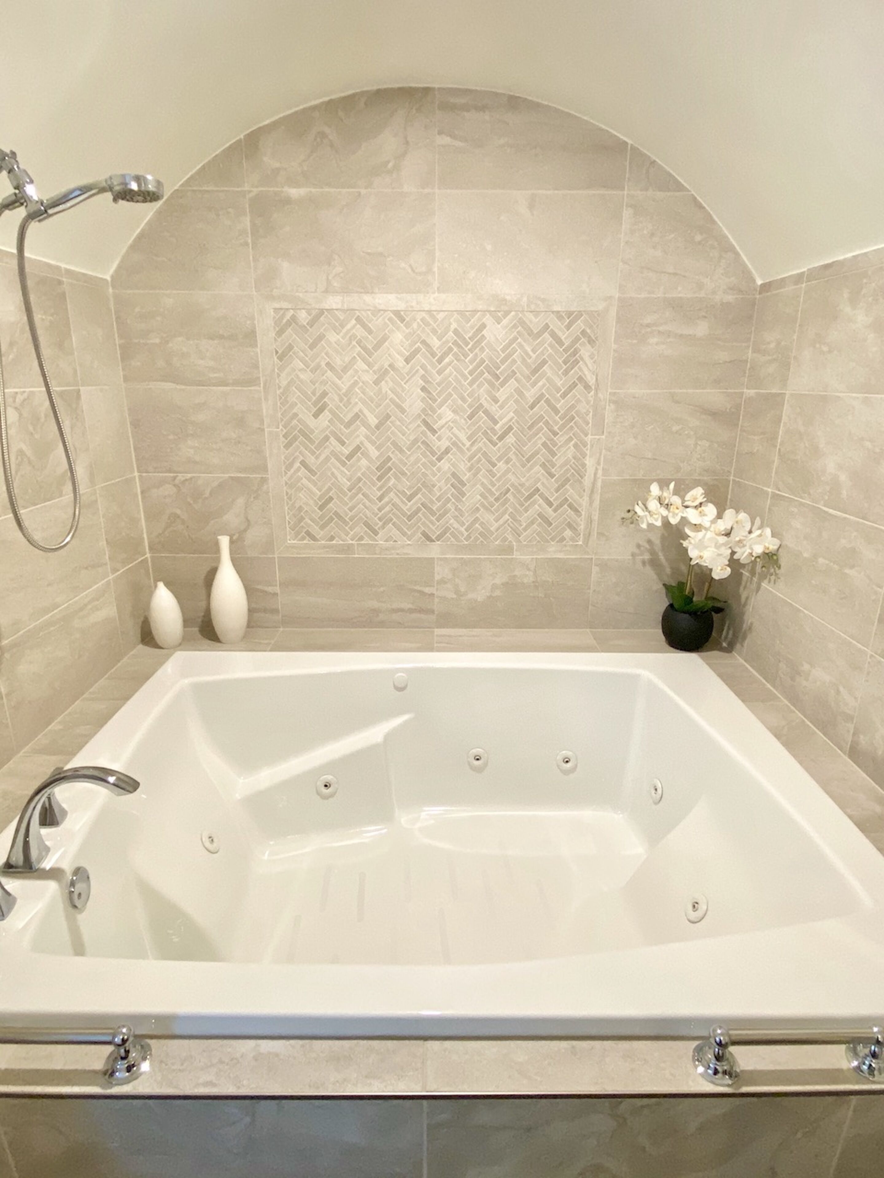 A modern bathroom with a freestanding bathtub, a showerhead, and a decorative herringbone tile backsplash.