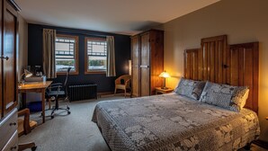 Een slaapkamer met een groot bed, een bureau met stoel, een raam met gordijnen en een radiator.