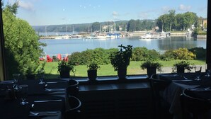 Een restaurant met terras aan een meer, met planten in potten en uitzicht op boten en groen.