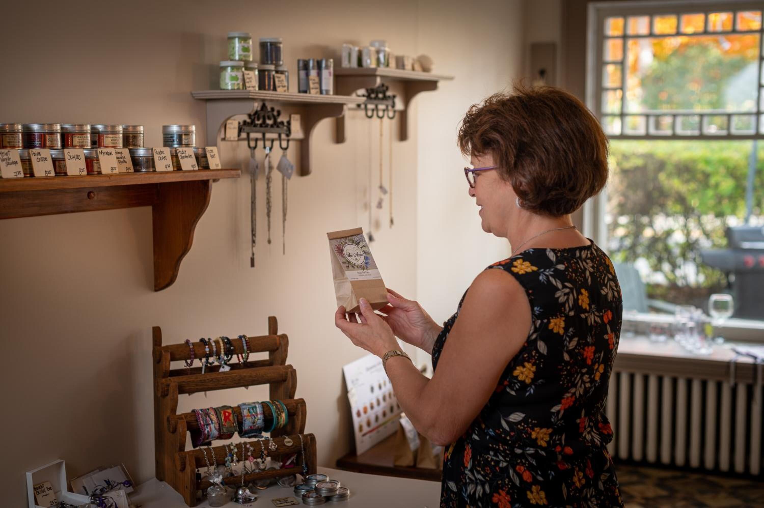 A woman examining a card in a room with shelves of jars and a jewelry display.