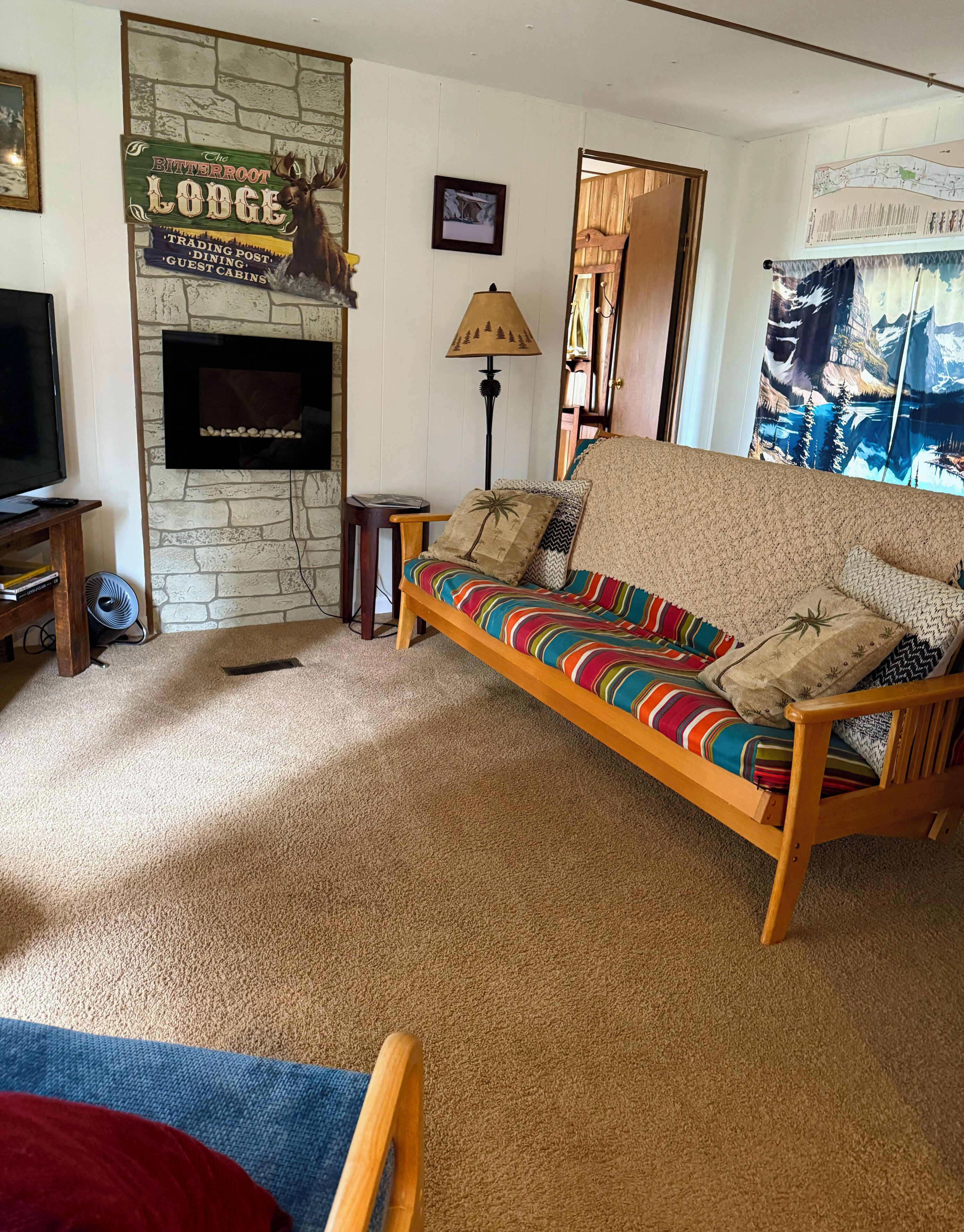 A cozy living room with a stone fireplace, a colorful sofa, a television, and a lamp.