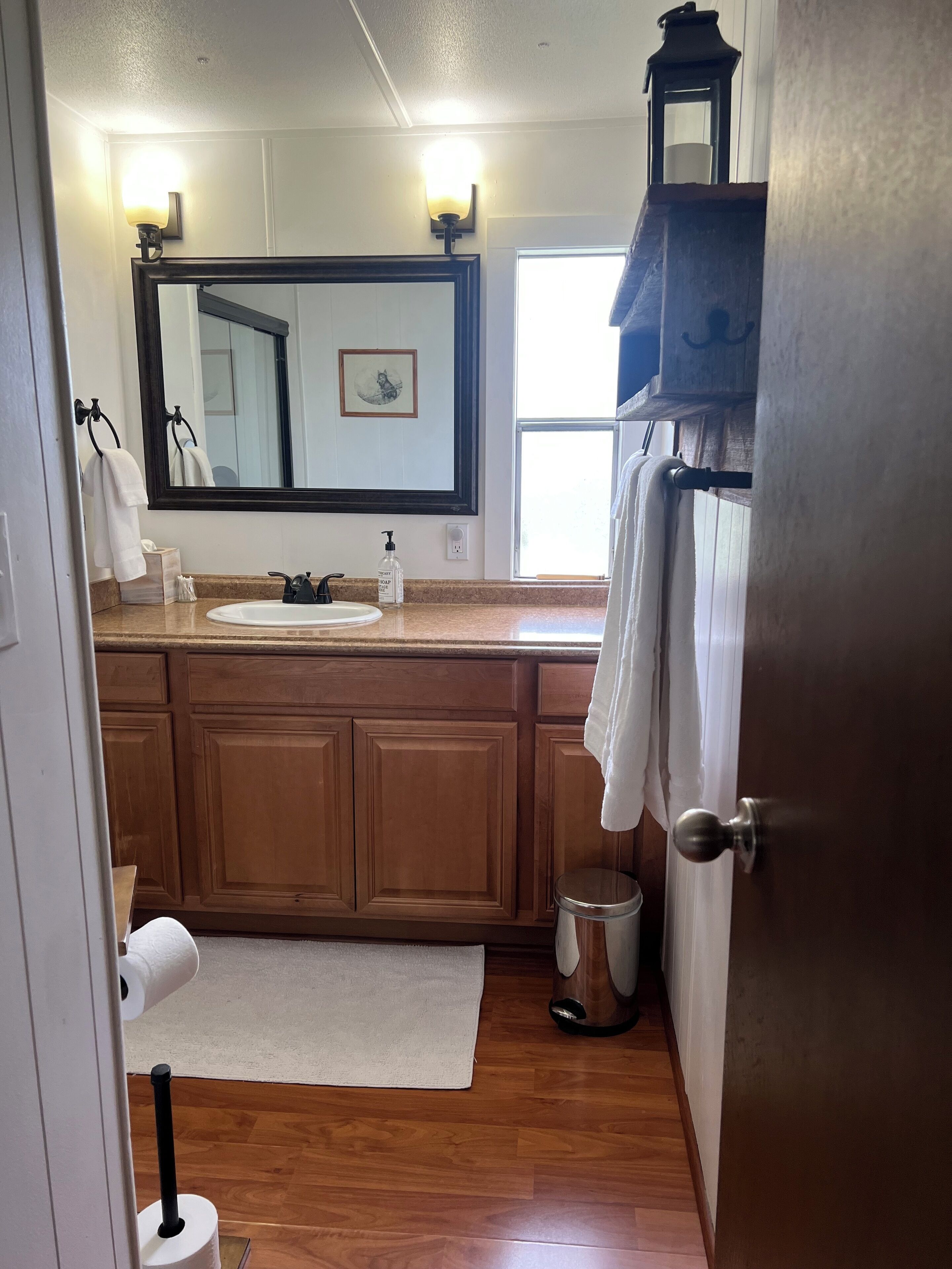 A bathroom with wooden cabinets, a sink, a mirror, a toilet paper holder, and a trash can.