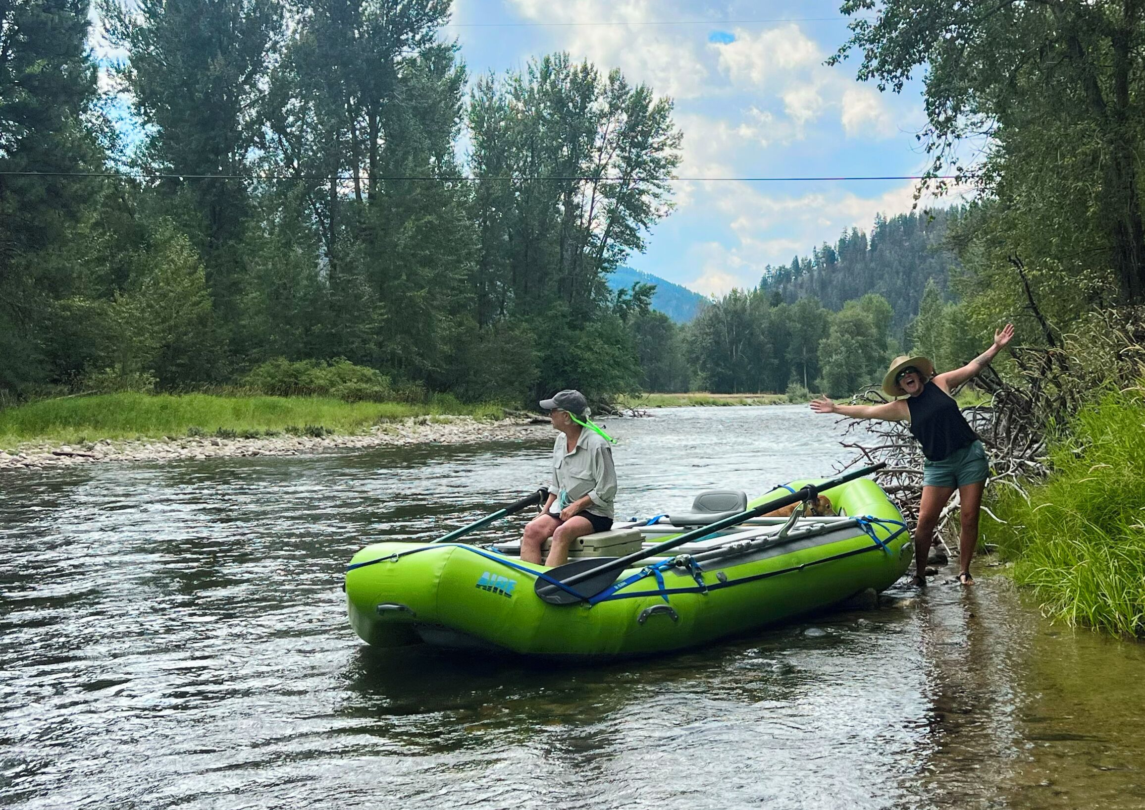A person in a green inflatable raft on a river surrounded by trees.