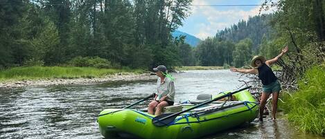 A person in a green inflatable raft on a river surrounded by trees.